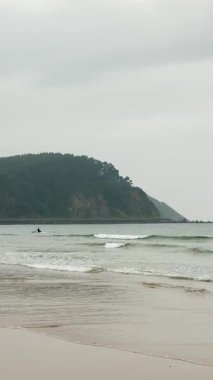 RIBADESELLA, İspanya - 17 Ağustos 2025 'te Ribadesella, İspanya' da kumsal, bulutlu hava altında kıyıya vuran dalgalar ve karamsar bir kıyı atmosferi.