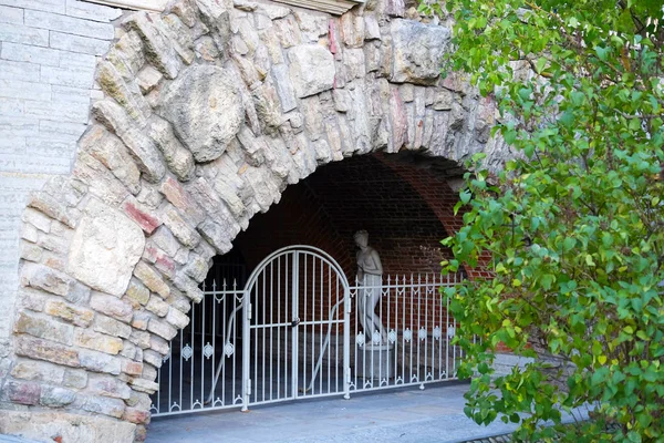 Stone arch with metal gates. In the depths of the arch is an abandoned stone figure