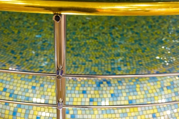 Chrome fence of the pool, promenade railing and the water pool as decor. Mosaic, interior design. Water surface.