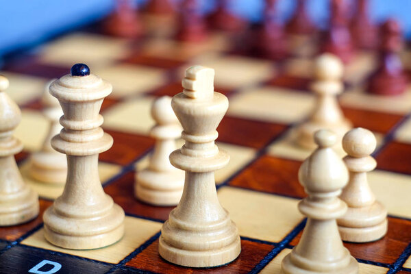 Color photo of chess Board and chess pieces, wooden chess pieces on the chessboard. White Queen and King in the foreground is a Soft focus. Blurred background. Flank