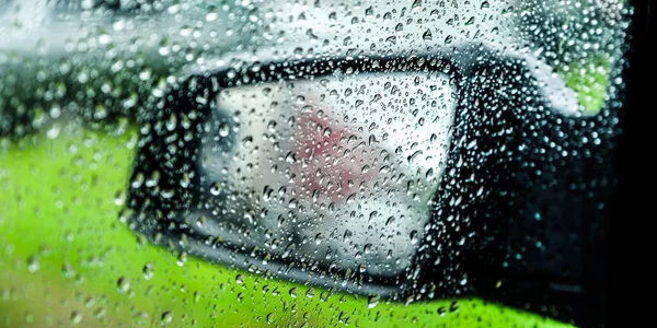 Water drops or rain drops on the car glass. Blurred background. Flank. Car mirror in the background.