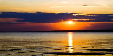 Denizin ve güneşin arka planda sakin dalgalar üzerinde şaşırtıcı altın yansıması ile onu yukarıda gökyüzü turuncu günbatımı toplayan yanan çok güzel. Sahilde muhteşem yaz gün batımı görünümü.