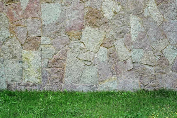 Texture masonry stone wall, green grass against the wall.