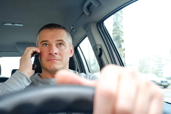 The man behind the wheel sitting in the car. Takes a phone call.