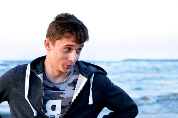 Free happy young man standing on the beach with his arms outstretched like a bird, feeling the warm wind looking into the distance, relaxed and carefree.