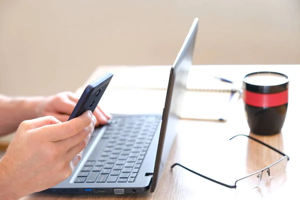 Smartphone dans les mains du mode SMS. Café en verre. Lunettes et cahier prêts à partir. Ordinateur portable sur une table lumineuse. Prêt pour l'opération. Concentration sélective . — Photo