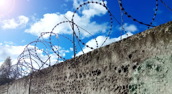 Alambre de púas en una cerca oscura. Contra un cielo azul con nubes . —  Fotos de Stock