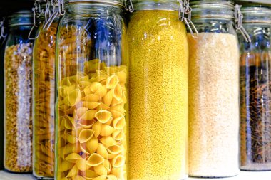 Various raw cereals, grains, beans and pasta for healthy cooking in glass jars on the kitchen shelf.Clean food, vegetarian, vegan, balanced diet concept clipart