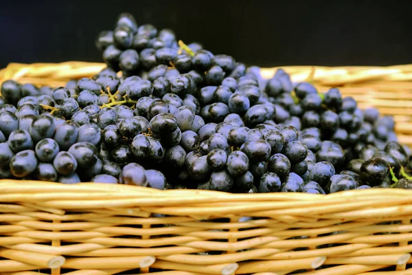 Ramas de uvas en una canasta de mimbre. Paquetes de uvas rojas maduras frescas en la tienda de comestibles, enfoque selectivo. Fondo de uva . — Foto de Stock