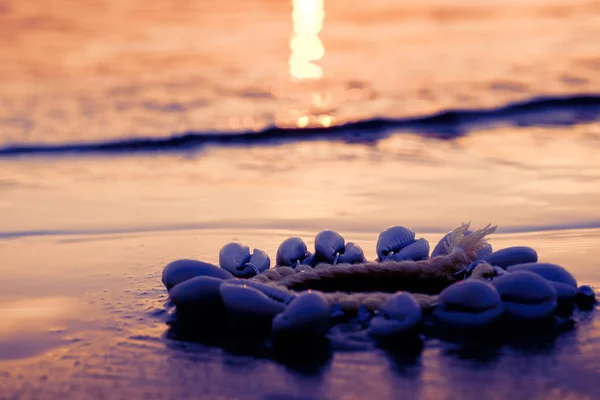 Pulsera de conchas en la arena. Contra el agua. Puesta de sol junto al mar. Fondo borroso . — Foto de Stock