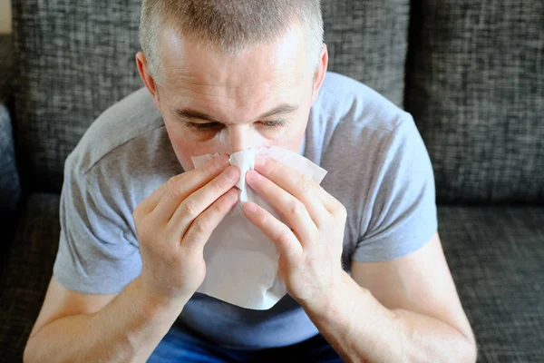 Un hombre con un pañuelo cerca de la nariz. Alergias, flores primaverales. Reacción al polen, síndrome alérgico . — Foto de Stock
