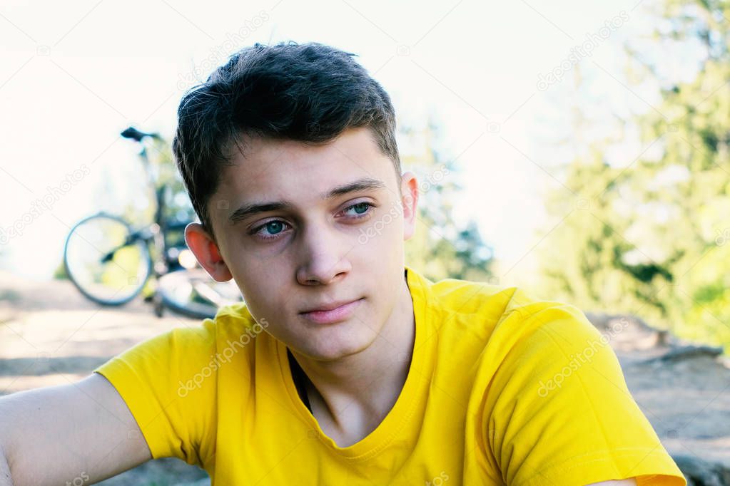 Young man sitting on the mountain near the bike. He looks dreamily into the distance. Sports lifestyle.