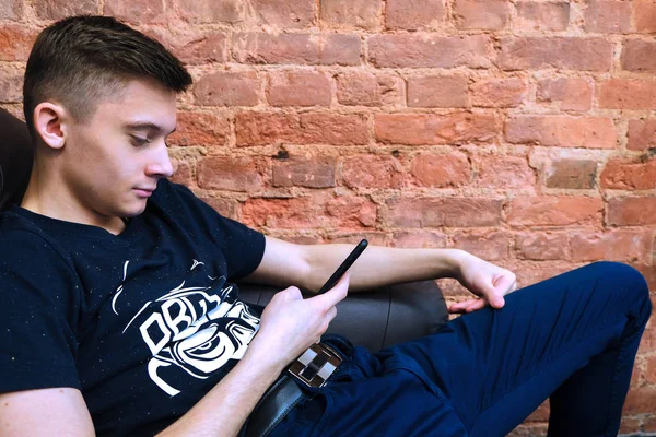뷰티 스튜디오. 소파에 앉아 있는 청년. 스마트폰에서 메시지를 읽습니다. 뉴스를 읽는 미소. — 스톡 사진