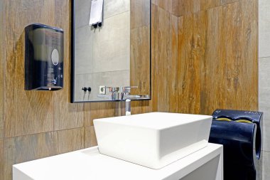 Havaalanının banyosundaki aynanın yanındaki lavabo. El mendilleri. Elektrikli el kurutma makinesi.