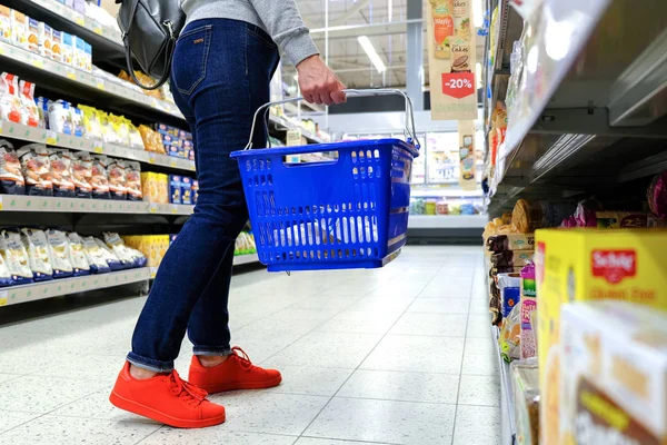 Eine Frau hält den Griff des Einkaufswagens in der Hand und geht den Gang im Supermarkt hinunter. kaufen Sie das Produkt. Saint-petersburg. Russland. 05. 20. 2019 — Stockfoto