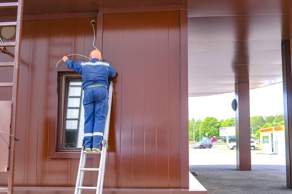 Elektroinstallateurmeister spannt ein elektrisches Kabel über das Fenster. auf einer Leiter stehend. — Stockfoto