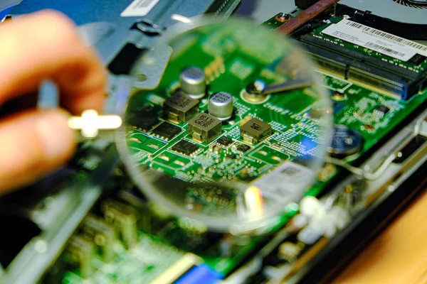 The motherboard is magnified through a magnifying glass. Hardware upgrades computer processor of the service component of the motherboard. The concept of support repair, equipment and PC industry. — Stock Photo, Image