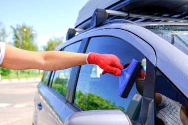 Lastik kazıyıcı olan bir adam arabayı yıkadıktan sonra camdan su kalıntılarını çıkarır. Araba yıkama. Self servis yıkama kompleksi. Yüksek basınçlı oto yıkama.