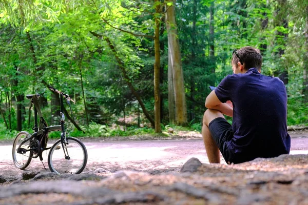 Młody mężczyzna siedzi na górze w pobliżu roweru. Wygląda marnie w oddali. Sportowy styl życia. — Zdjęcie stockowe