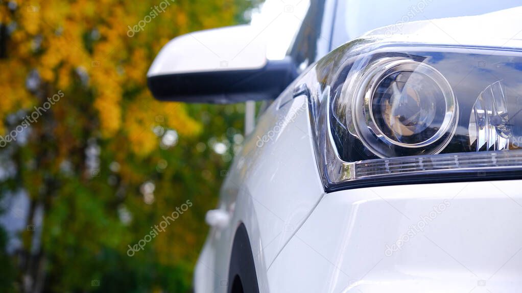 Car front view close-up on the background of a Park alley. Headlight glass. Background design. Detail of modern car headlights.