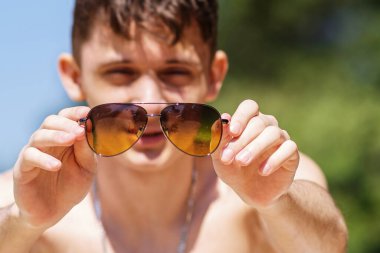 Neşeli bir adamın portresi. Güneşli bir sahilde rahatlıyor ve eğleniyor. Elde güneş gözlüğü. Seçici odaklanma. Bulanık plan