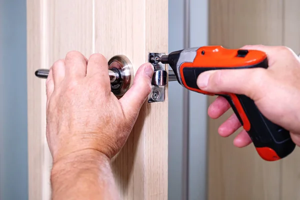 Repair of the door handle. The master clamps the loose screw with an electric screwdriver. — Stock Photo, Image
