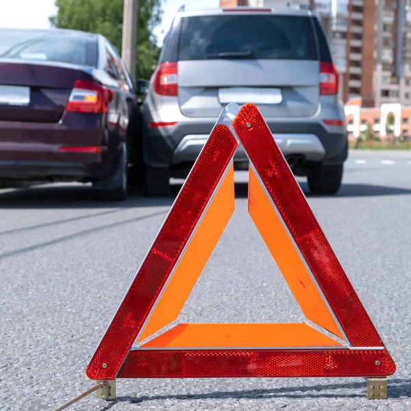 Triangular red retro-reflective sign of accident on the road. Collision of two cars. Broken bumper and hood. Car accident on the street