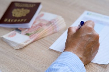 Bir kişi sigorta yaptırır ve anketi geçer. Masanın üzerinde bir pasaport ve bir tomar banknot var.