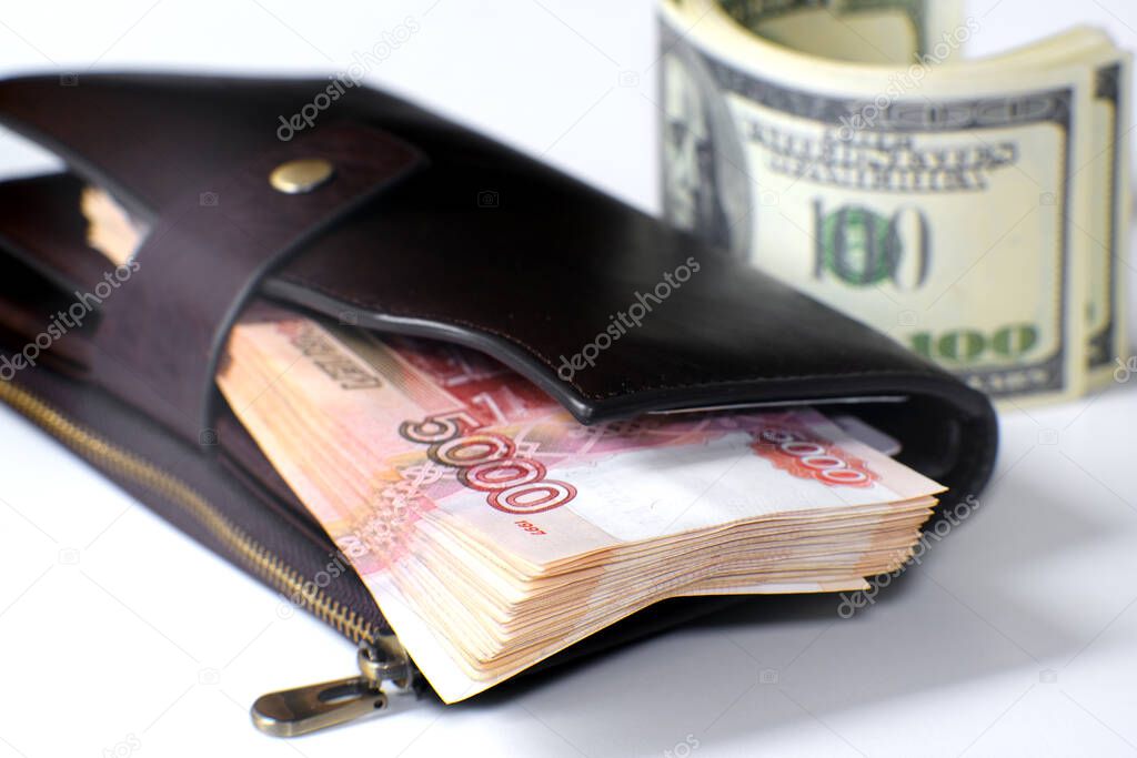 A bundle of banknotes in a leather wallet. Next to it is a stack of hundred-dollar bills.