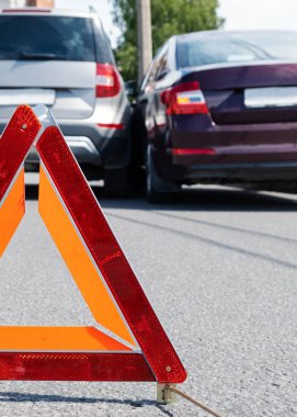 Üçgen kırmızı retro yansıtıcı yol kazası işareti. İki arabanın çarpışması. Tampon ve kaput kırılmış. Sokakta araba kazası..
