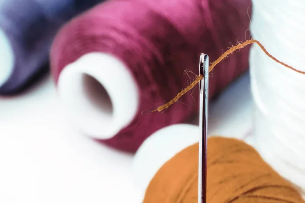 Multi-colored sewing threads. Spools of thread. Needle with thread in the eye of the needle.