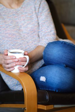 Kız elinde bir fincan kahve tutuyordu. Ellerini ısıtır. Evde, karantinada bir sandalyede oturmak.
