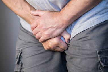 Bir adam iki eliyle kasığını tutar, idrar kesesinde ürolojik bir ağrı nöbeti geçirir.
