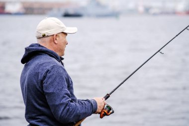 Elinde olta kamışı olan beyzbol şapkalı bir balıkçı gülümsüyor. Sağlıklı açık hava eğlencesi kavramı