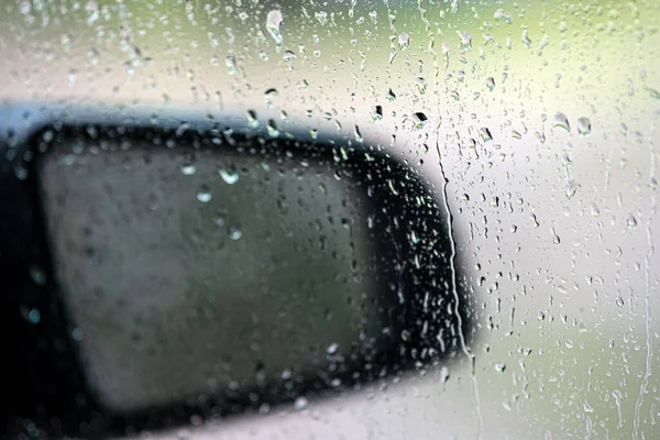 Raindrops on the car window. The rearview mirror is out of focus, bokeh