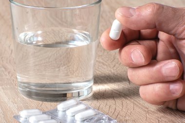 Elinde tablet, reçeteli ilaç alıyor. Masanın üzerinde bir bardak su var. Modern tıp