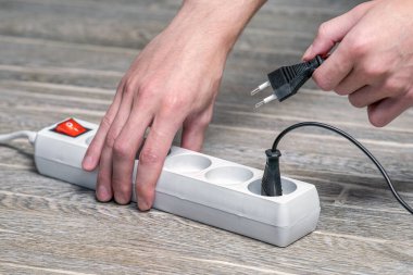 Ev sahibesi elinde fitili olan bir elektrik uzatma kablosu tutuyor ve cihazı prize bağlıyor.