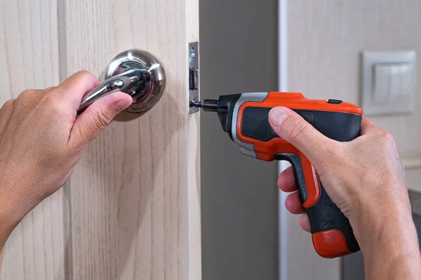 Repair of the door handle. The master clamps the loose screw with an electric screwdriver