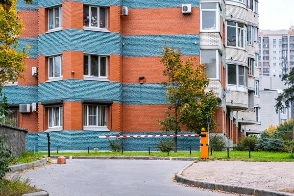 Automatic barrier of orange color with a white stripe and red warning stripes, for the entry of cars. Entrance to the courtyard of an elite residential complex