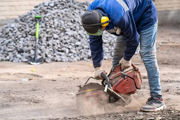 Construction worker in safety glasses and noise-canceling headphones at work. Cutting concrete floor for cable laying with a diamond cutting machine