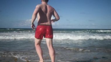 Genç adam okyanusun dalgalarına doğru koşar.