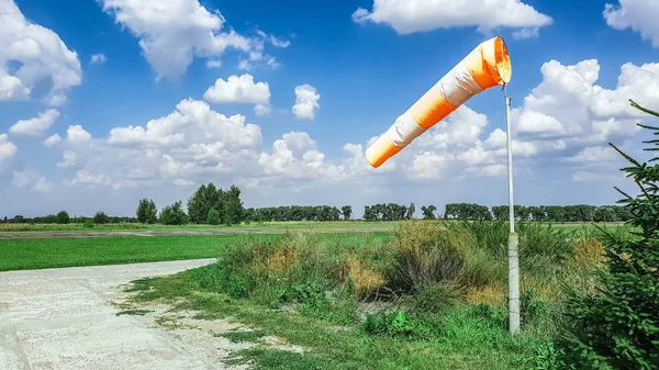 red-white wind direction on the blue sky background on the aerodrome, green field and clouds