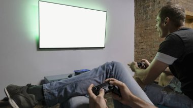 İki adam bilgisayar oyunu Pro Evolution Soccer oynamak. Konsol denetleyici holding eller. Futbol ya da futbol oyun televizyon. Geniş ekran tv asmak duvar