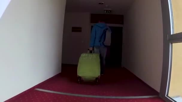 スーツケースとブルーのジャケットの男性が部屋にチェックインするホテルの廊下を歩いています — ストック動画