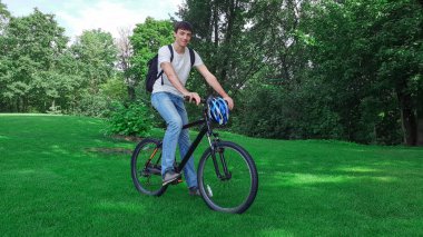Çekici genç adam yeşil çimlerin arkasında bisikletin üzerinde oturuyor.