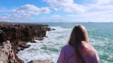 Güneşli havalarda buzlu çökmesini güçlü okyanus dalgaları. Saf güç, sergi doğanın zorlar. Güçlü enerji. Okyanus güç Dünya'ya karşı. Bir uçurum Okyanusu yakın oturan ve dalgaları seyretmekten sarışın genç kadın