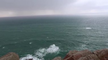Okyanus dalgalar kayalar üzerine çökmesini. Mavi dalgalar, beyaz köpük ve kayalar ile deniz manzarası. Ufuk uçurumun üzerinden bir bakış. Bulutlu hava