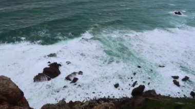 Okyanus dalgalar kayalar üzerine çökmesini. Mavi dalgalar, beyaz köpük ve kayalar ile deniz manzarası. Ufuk uçurumun üzerinden bir bakış. Bulutlu hava