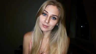 karanlık bir arka plan üzerinde parlak mavi gözlü güzel sarışın kadın kamera ile gülümseyen ve flört flört ediyor