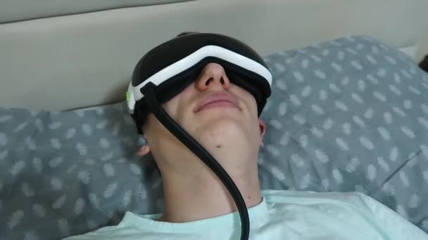 Giovane Uomo Attraente Utilizza Dispositivo Massaggio Oculare Sdraiato Sul Letto — Video Stock